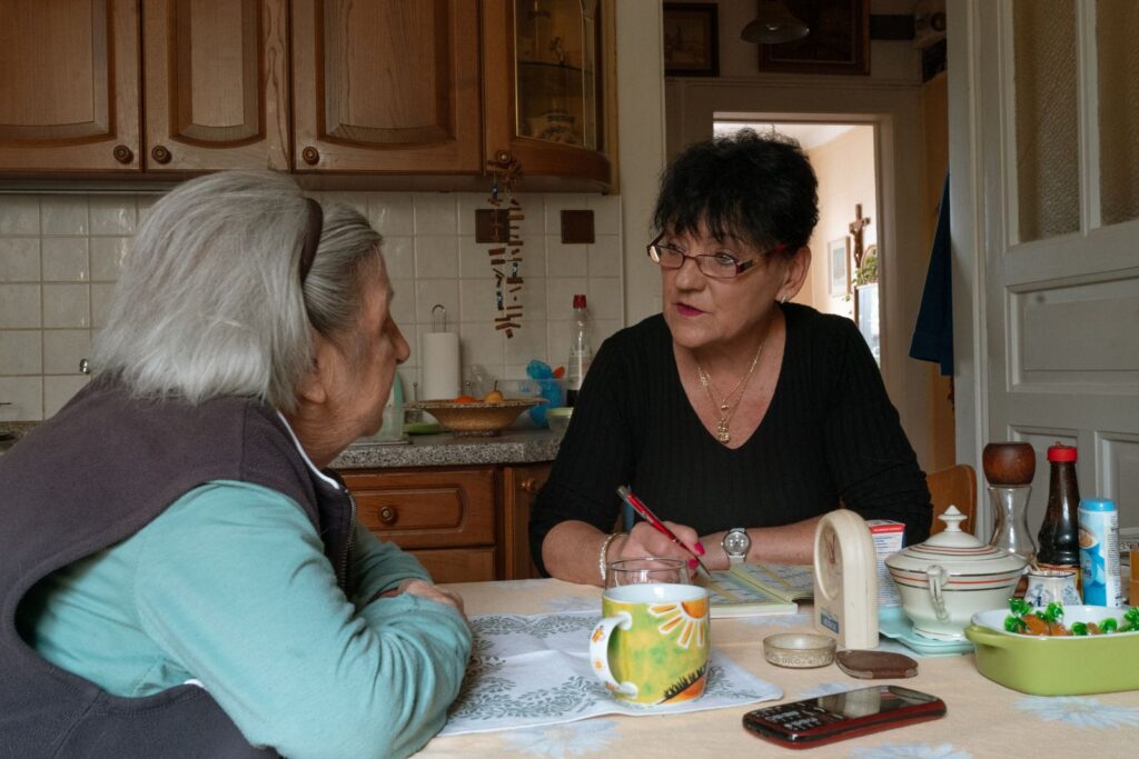 A caregiver and an older woman going through paperwork together at a kitchen table