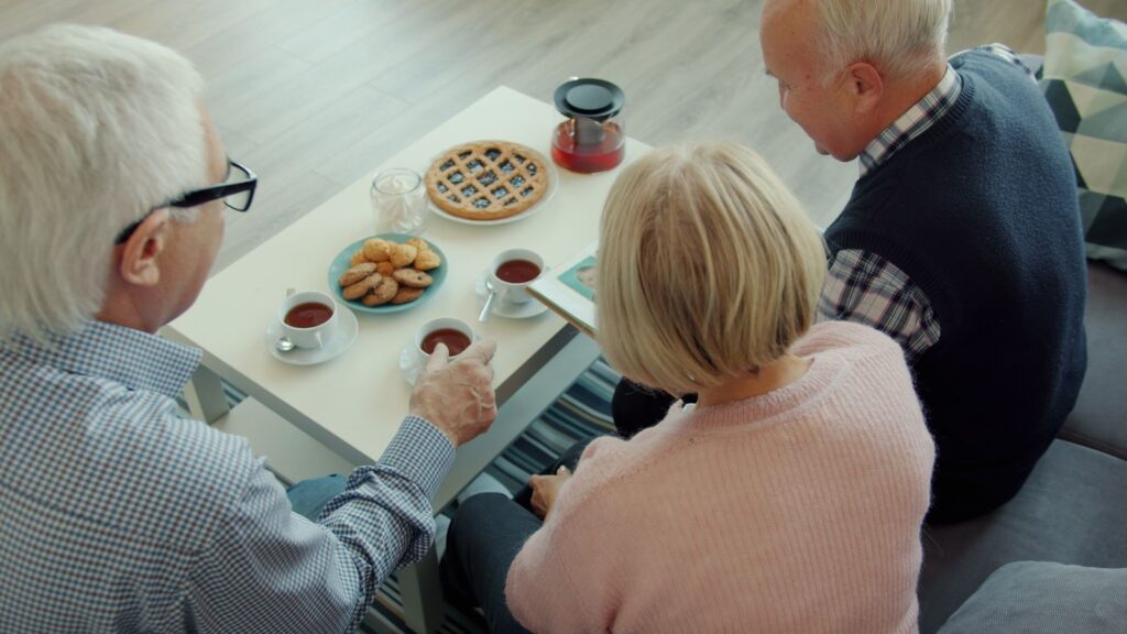 Older friends sitting together over tea and biscuits at a kitchen table