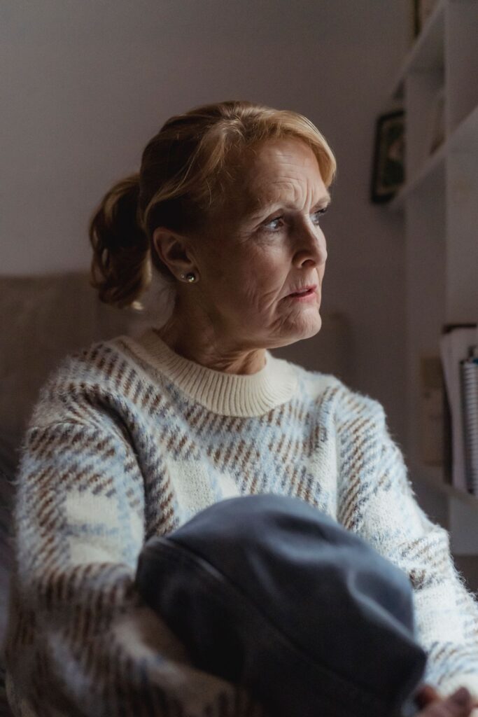 An older woman sitting quietly at home, looking away in thought