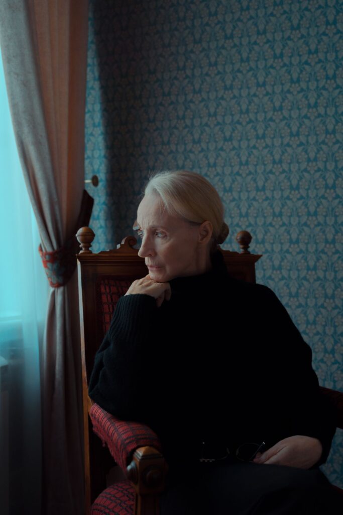 An older woman sitting in an armchair beside a window at home